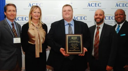 Five people standing together at an award event, one person holding a plaque.