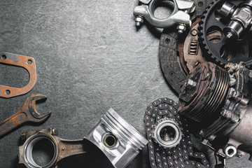 Assorted mechanical parts including gears, a piston, a gasket, and a wrench arranged on a textured surface.