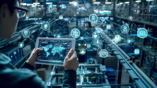 Person holding a tablet in a factory setting, viewing a digital interface with various connected icons representing technology and industrial concepts.
