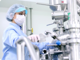 A person in protective gear operates machinery in a sterile laboratory environment.