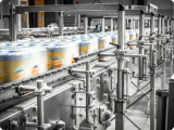 A moving conveyor belt with blurred stacks of packaged products in a factory setting.