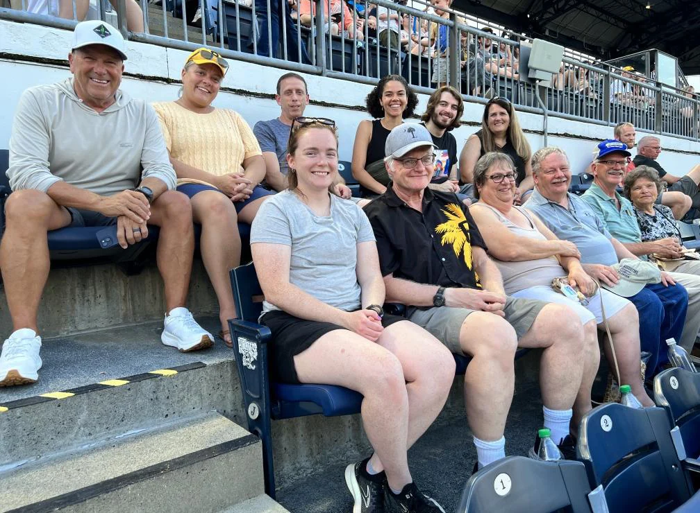 Group of people sitting in stadium seats, smiling.
