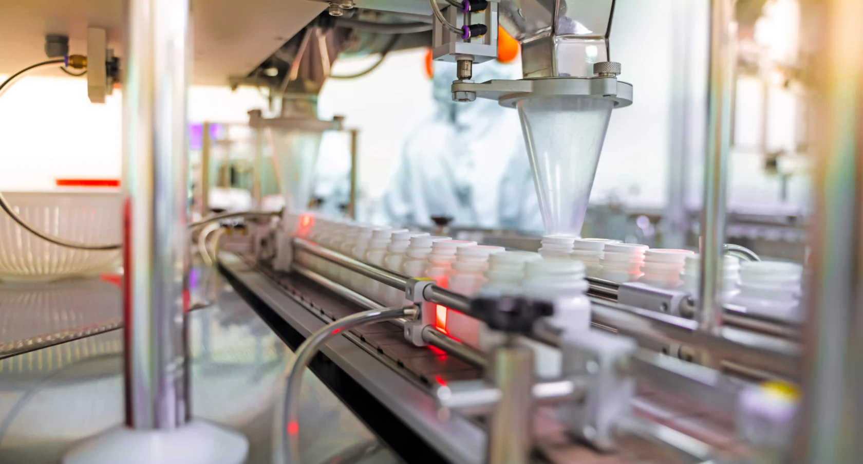 Close-up of an automated production line with machinery filling white plastic bottles, likely in a pharmaceutical or manufacturing setting.