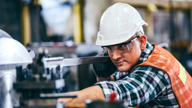 Worker in safety gear, including hard hat and goggles, operates heavy machinery in an industrial setting.
