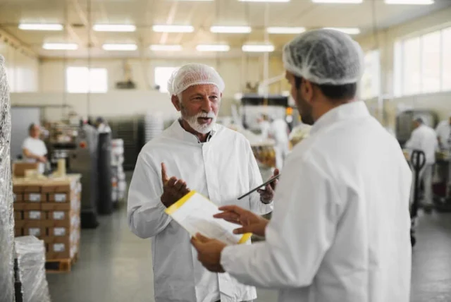 Two serious business men in sterile clothing standing in a food manufacturing factory.