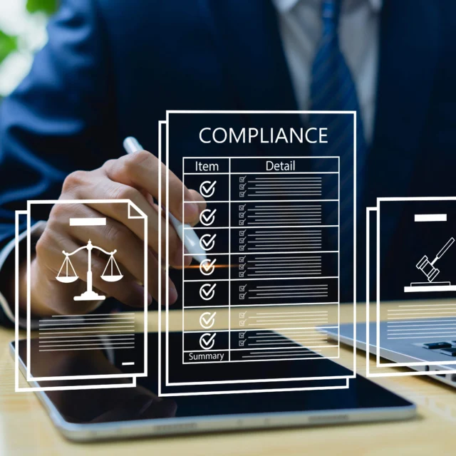 A person in a suit works on a laptop and tablet, with digital graphics showing compliance checklists and legal icons overlayed.