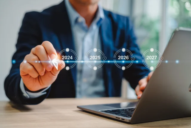 A person in a suit uses a laptop and touches a virtual timeline displaying the years 2024, 2025, 2026, and 2027.
