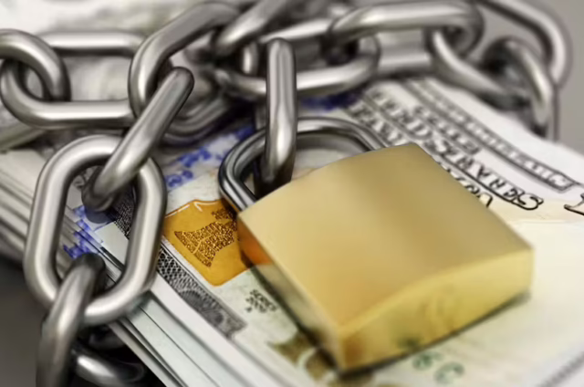 Stack of U.S. hundred-dollar bills wrapped in a thick chain and secured with a gold padlock.